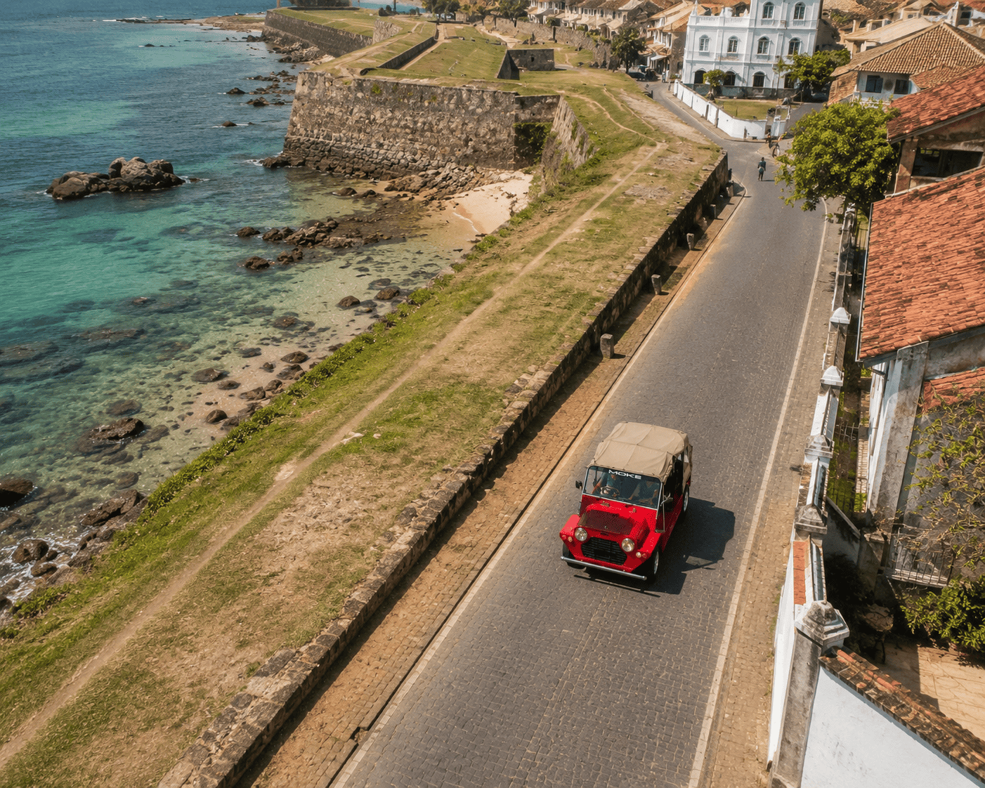 A vintage red Mini Moke driving along the ramparts of Galle Fort with the ocean beyond