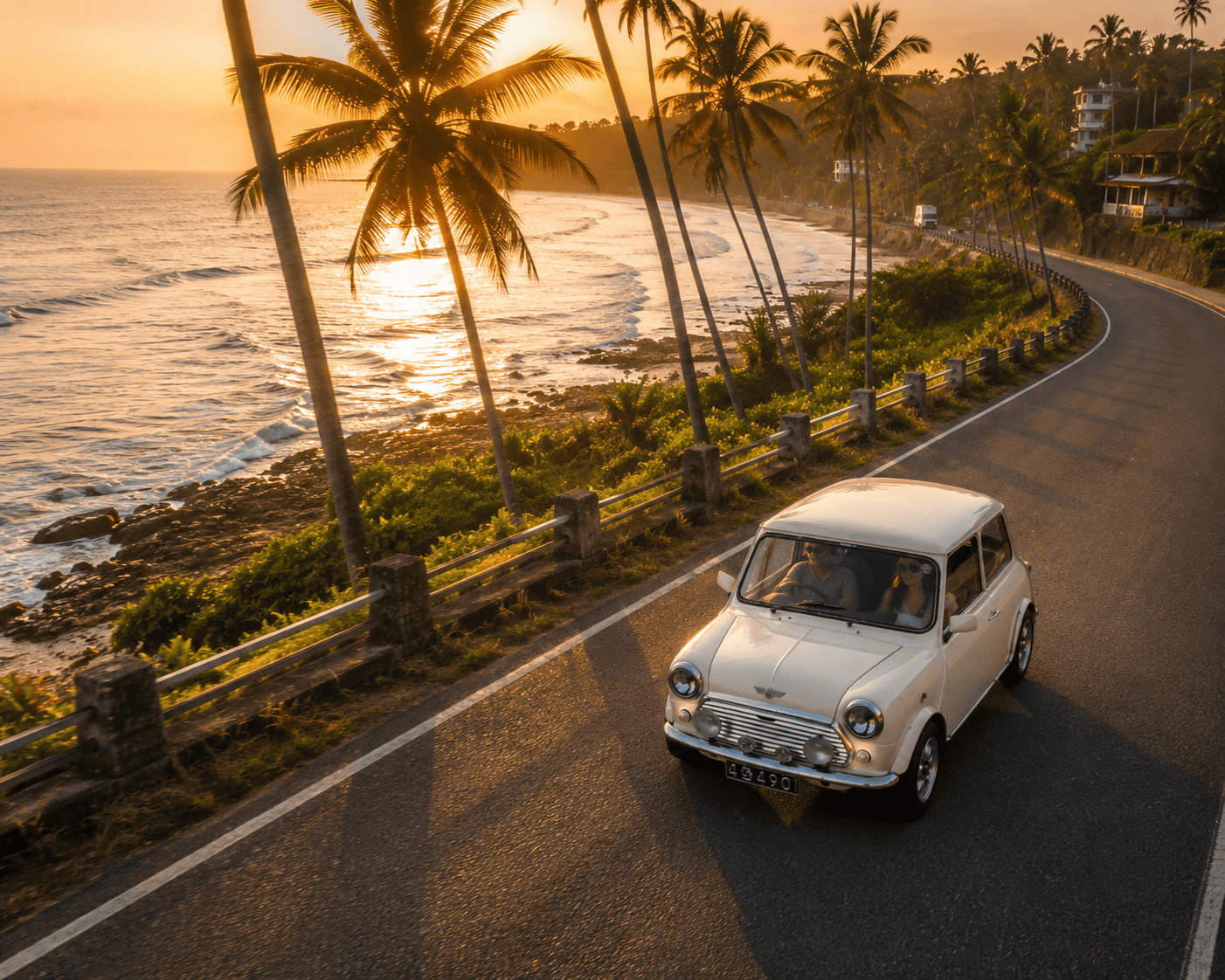 A vintage white Mini Cooper driving along a coastal road at golden hour with the sunset over the ocean